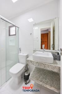 a white bathroom with a toilet and a sink at Apartamento espaçoso com ar condicionado e Wi-fi, a 100 metros da praia - Edifício Estoril in Ubatuba