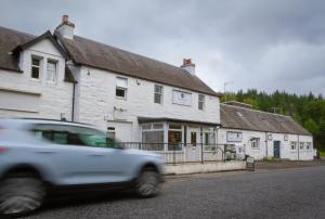 un'auto bianca che passa davanti a un edificio bianco di The Ballinluig Inn a Pitlochry