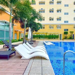 einem Hotelpool mit weißen Stühlen und einem Gebäude in der Unterkunft J&A Cozy Calm Stay in Biñan