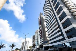 ein hohes weißes Gebäude mit Palmen davor in der Unterkunft Cobertura duplex de frente pro mar in Natal