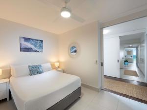 a white bedroom with a bed and a large mirror at Grand Mercure Apartments Magnetic Island in Nelly Bay