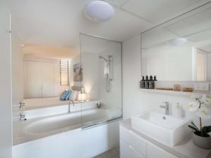 a white bathroom with a tub and a sink at Grand Mercure Apartments Magnetic Island in Nelly Bay