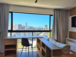 een woonkamer met een bureau en een groot raam bij CURTA! |165| Lindo Studio | Próx Centro de Eventos in Balneário Camboriú +16 foto's