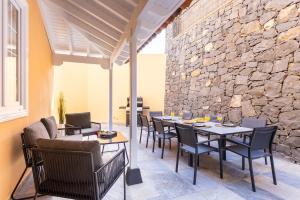 Un patio con mesas y sillas y un muro de piedra. en Zafiro Piscina Climatizada Jacuzzi Barbacoa Vistas al mar, en La Orotava