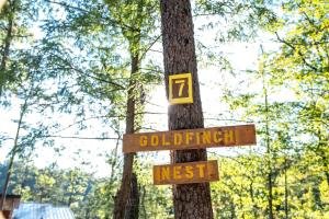 a wooden sign on a tree in a forest at The Goldfinch's Nest - Glamping Tent with AC in Rogers