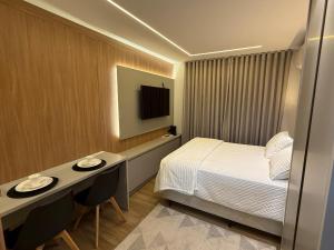 a hotel room with a bed and a desk and a tv at Studio Novo Moderno e Aconchegante - Centro in Paranaguá
