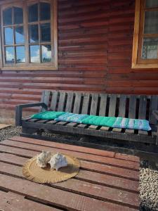 eine Holzbank mit grünen Kissen und einem Hut darauf in der Unterkunft Cabaña AlbaMarina - Pichilemu in Pichilemu + 2 Fotos