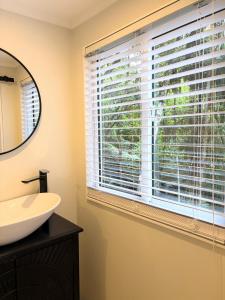 Un baño con ventana con persianas y lavabo en Tui Bush Chalet, en Parakakau