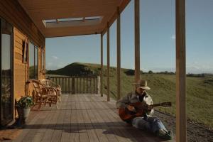 un hombre sentado en un porche tocando una guitarra en Sunsets, outdoor bath, mountain views, fire pit, en Marotiri