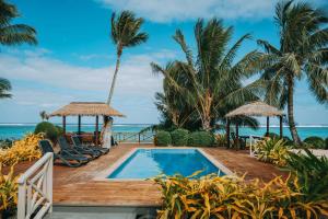 a resort pool with chairs and palm trees and the ocean at Moana Sands Beachfront Villas in Rarotonga