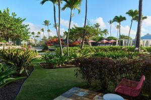 un giardino con palme e un prato con una sedia rosa di OUTRIGGER Kaua'i Beach Resort & Spa a Lihue