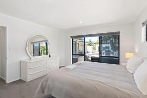 a white bedroom with a large bed and a mirror at Beach Escape Papamoa in Papamoa