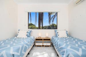 a bedroom with two beds and a window with palm trees at Esplanade Charm Apartment in Torquay