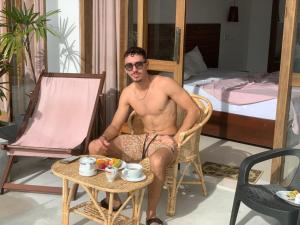 a man sitting in a chair with a table at Plantation Inn in Weligama