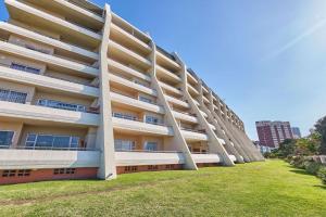 an apartment building with white balconies and a grass field at 102 L'escalier CABANAS-ON THE BEACH in Amanzimtoti