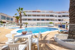 a swimming pool with a table and chairs and a building at Azahara Beach in Arona