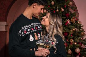 a man and woman holding wine glasses in front of a christmas tree at Opinione Dimora Storica & Private Spa in San Lorenzo in Banale