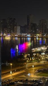 a city at night with a fountain in the water at Single bed space - Al Majaz 2 in Jazīrat al Ḩibāb