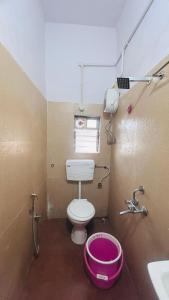a bathroom with a toilet and a pink bucket at Hotel Cozy Inn in Kālundri