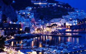 una città illuminata di notte con barche in acqua di Confort holiday in Sorrento a Sorrento