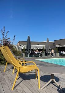 Zwei gelbe Stühle und ein Tisch neben einem Pool in der Unterkunft Novotel Reims Tinqueux in Reims
