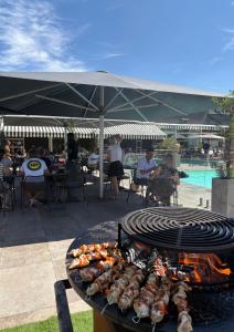 Ein Grill mit Essen darauf, unter dem Menschen unter einem Sonnenschirm sitzen in der Unterkunft Novotel Reims Tinqueux in Reims