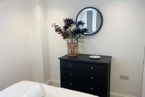 eine schwarze Kommode mit einem Spiegel und eine Vase mit Blumen in der Unterkunft Relaxing 1 bed apartment on Tetbury High St in Tetbury