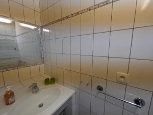 ein weiß gefliestes Badezimmer mit Waschbecken und Spiegel in der Unterkunft Lys in Bourbonne-les-Bains + 6 Fotos