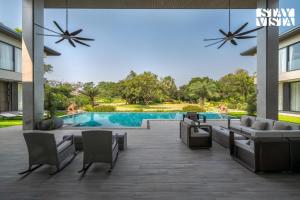 an outdoor patio with a pool and chairs and a building at StayVista at Acasa with Lawn in Alibaug