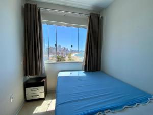 Un dormitorio con una cama azul y una gran ventana. en Apto Confortável p/ até 9P, 50mts do mar Piçarras, en Piçarras