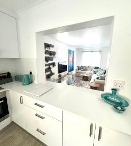 Blue Beach Haven في Cape Town: مطبخ مع دواليب بيضاء وغرفة معيشة