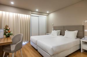 a bedroom with a large white bed and a desk and a chair at Hotel Cristal Caldas in Caldas da Rainha