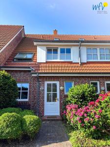 万根沃格Ferienhäuser Jadehörn Ferienhaus Dünen Hus的砖屋,有白色门和粉红色的花