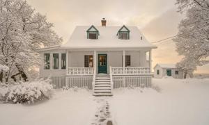 ein weißes Haus mit grüner Tür im Schnee in der Unterkunft Quietude by the River - La dependance sur les battures in Notre-Dame-du-Portage