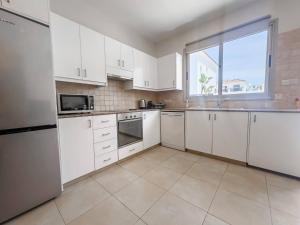 a kitchen with white cabinets and a large window at Pernera Seaside Villa - Sun, Sea, Poolside Bliss in Protaras