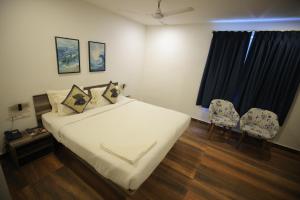 ein Schlafzimmer mit einem Bett und zwei Stühlen und einem Fenster in der Unterkunft Hillside Aqua in Bhubaneshwar