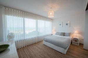 a white bedroom with a bed and large windows at Oceana - A Panoramic Beachfront Escape for Groups in Port Elliot