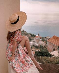 a woman wearing a hat sitting on a ledge looking at a city at La Dolce Vita Ravello - Exclusive Family & Group Villa with 4 Apartments, 5 Bedrooms in Ravello