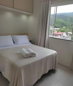 una camera da letto con un letto bianco con asciugamani sopra di Apartamento Harmonia 402 a Pomerode