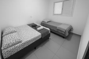 two beds in a white room with a window at Apto Novo com Ar e Wi-Fi Perto da UFU Monte Carmelo in Monte Carmelo