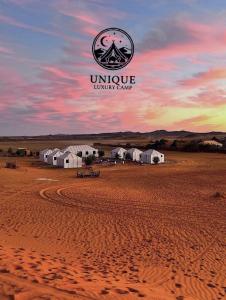 Unique Luxury Camp في مرزوقة: مجموعة من الخيام في الصحراء مع غروب الشمس