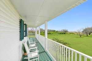 eine Veranda mit zwei weißen Stühlen und ein Feld in der Unterkunft Waterfront Getaway • Balcony + Bayou Views in Lafitte