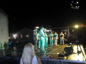 un grupo de personas de pie alrededor de un escenario por la noche en Apartment Selman, en Nin