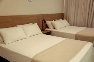 two beds in a hotel room with white sheets at Hotel Premier Janauba in Janaúba +2 photos