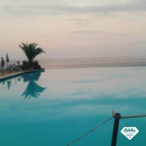 una piscina con una palma e l'oceano di Delle Zagare Apartments ad Alcamo Marina