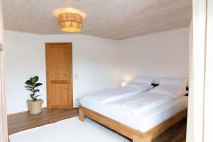 una camera da letto con un letto con lenzuola bianche e un soffitto in legno di Gemütliche Ferienwohnung am Kochelsee a Schlehdorf