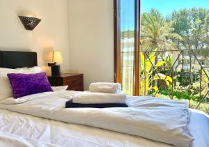 a bed with white sheets and purple pillows and a window at Beachhouse 2min to the sea with pool & wonderful garden in Calvia Town