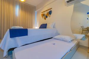 um quarto com uma cama com lençóis brancos e almofadas azuis em Nossa Praia Flats - Açores 109 Piscina Vista Panorâmica em Tamandaré mais 33 fotografias