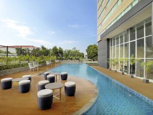 uma piscina com bancos e mesas e um edifício em Mercure Makassar Nexa Pettarani em Macáçar
