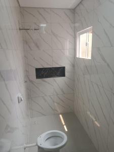 Un baño blanco con inodoro y ventana. en Apartamento Confortável Novo com Ar condicionado, en Tangará da Serra